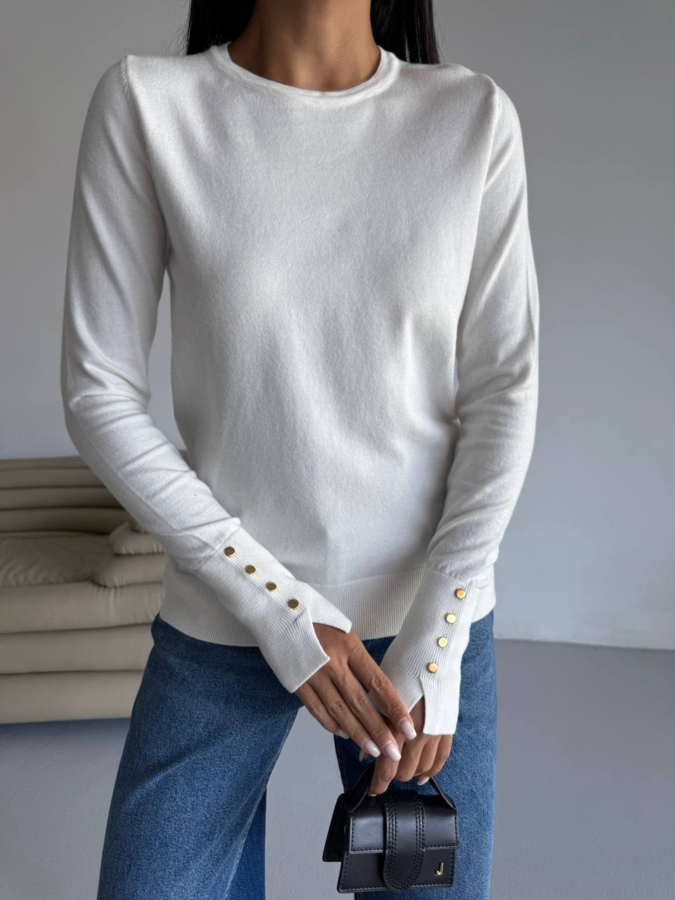 White long-sleeve top with button details worn by a person, holding a small black handbag.