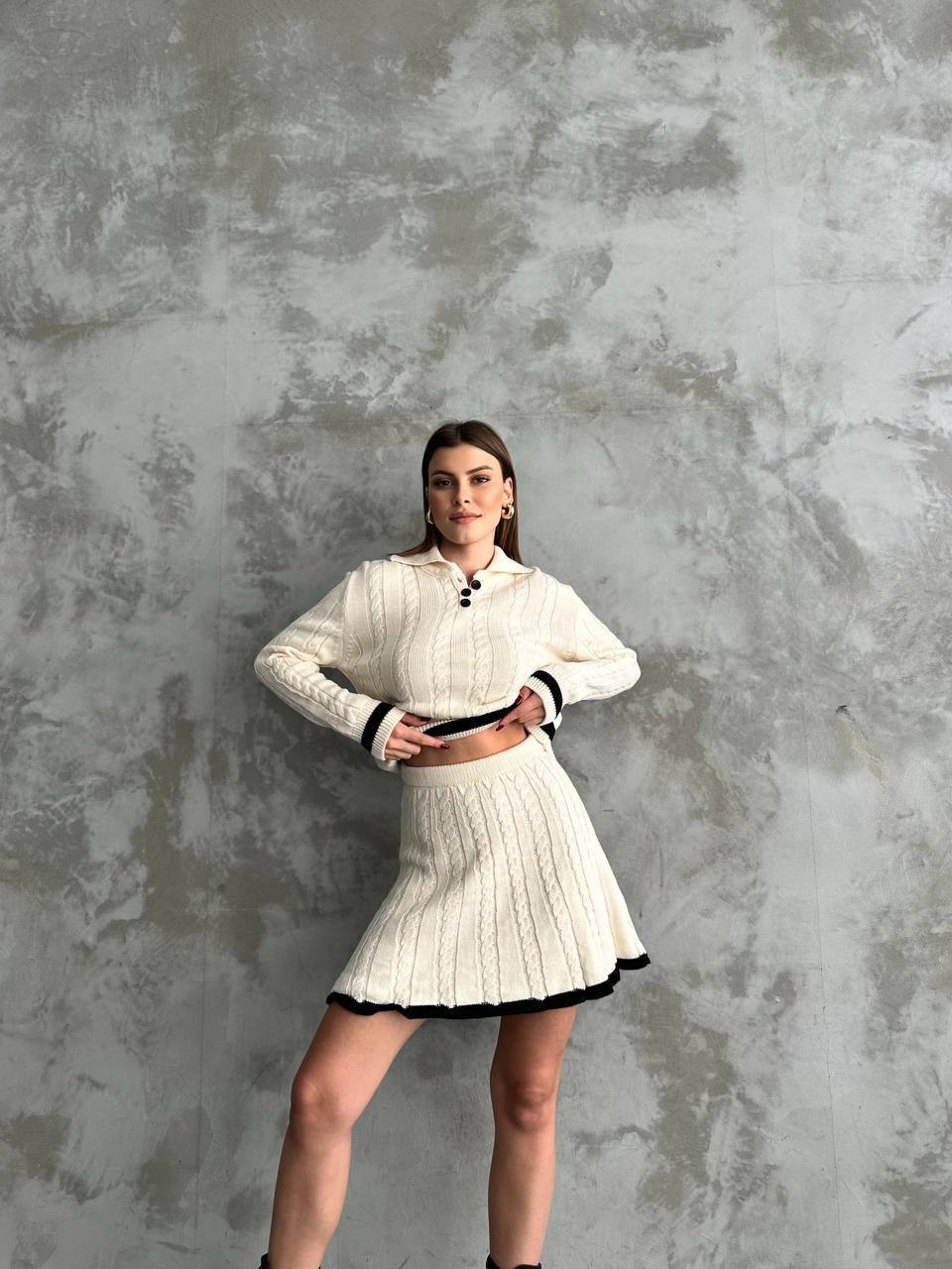 Woman wearing a white knit outfit against a textured gray wall