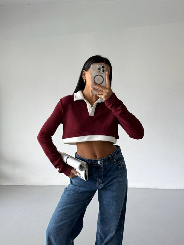 Person wearing a burgundy sweater with white collar and blue jeans, taking a mirror selfie.