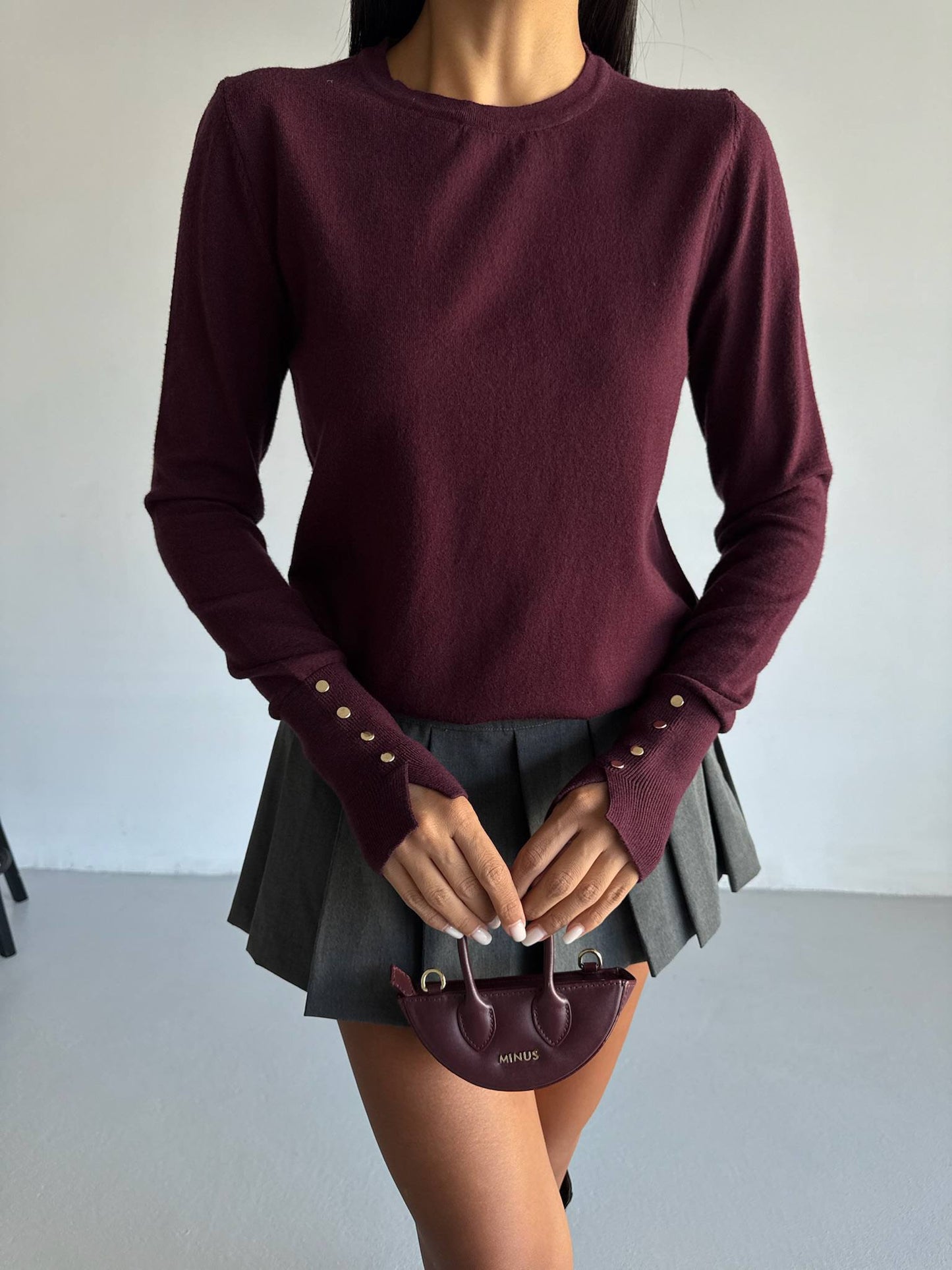 Person wearing a burgundy long-sleeve top and black skirt holding a matching handbag.
