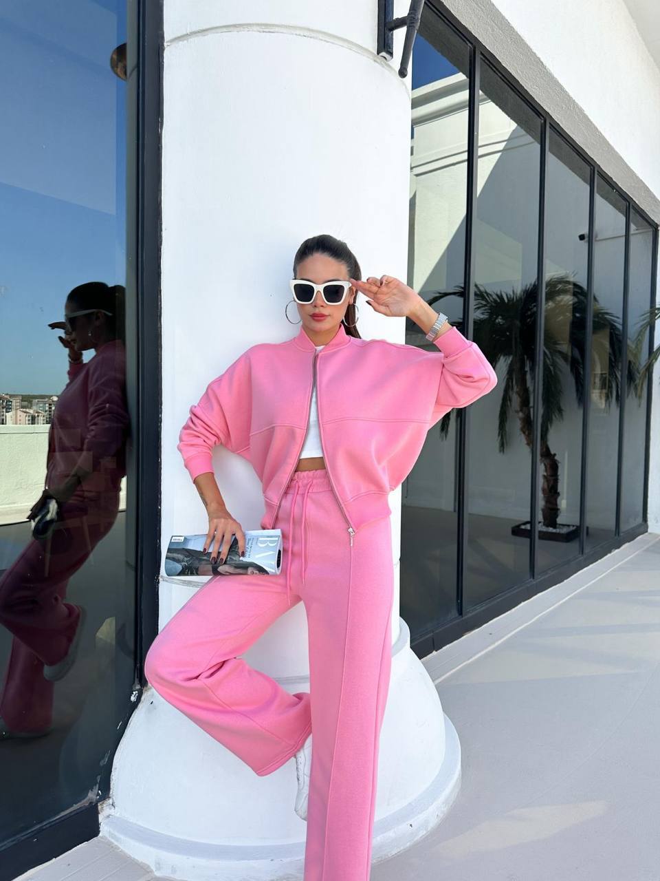 Person in a pink outfit posing on a white pedestal with a reflective surface and building in the background.
