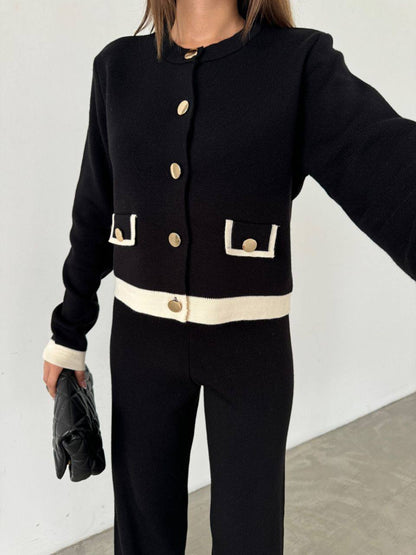 Person wearing a black jacket with gold buttons and a white shirt, standing against a plain background.