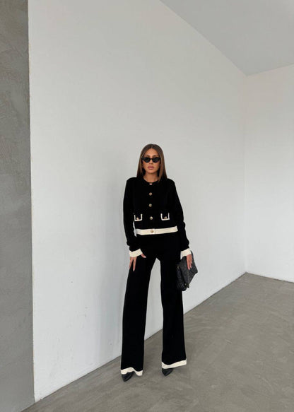 Person wearing a black outfit with white accents in a minimalistic room.