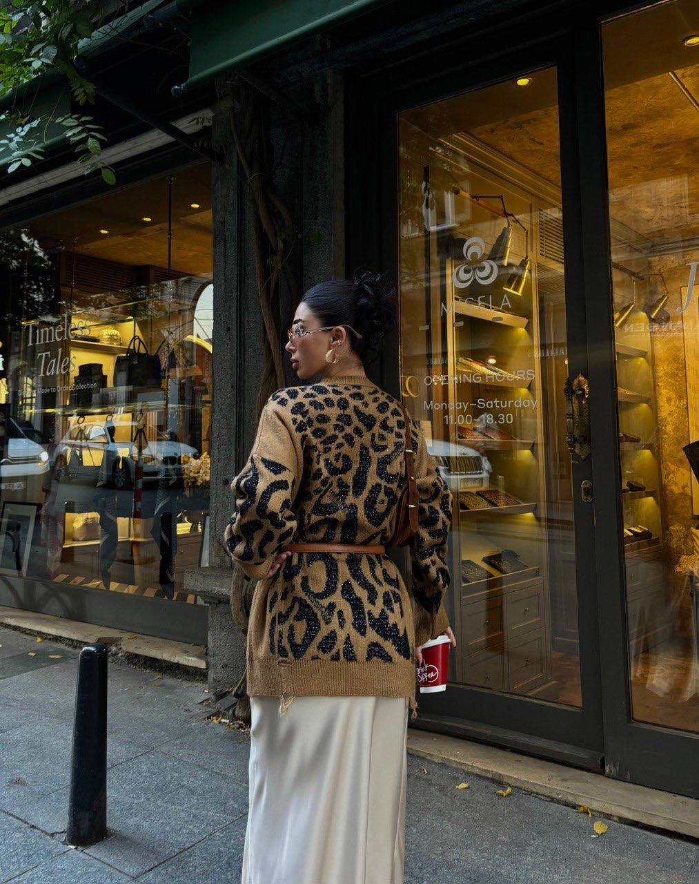Person wearing a leopard print coat standing outside a store with a glass door.