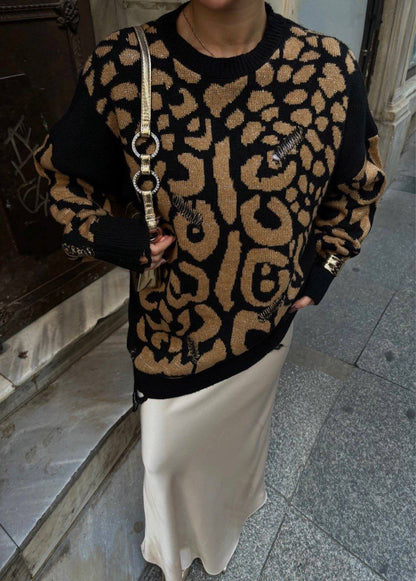 Person wearing a leopard print sweater and holding a handbag on a city street.