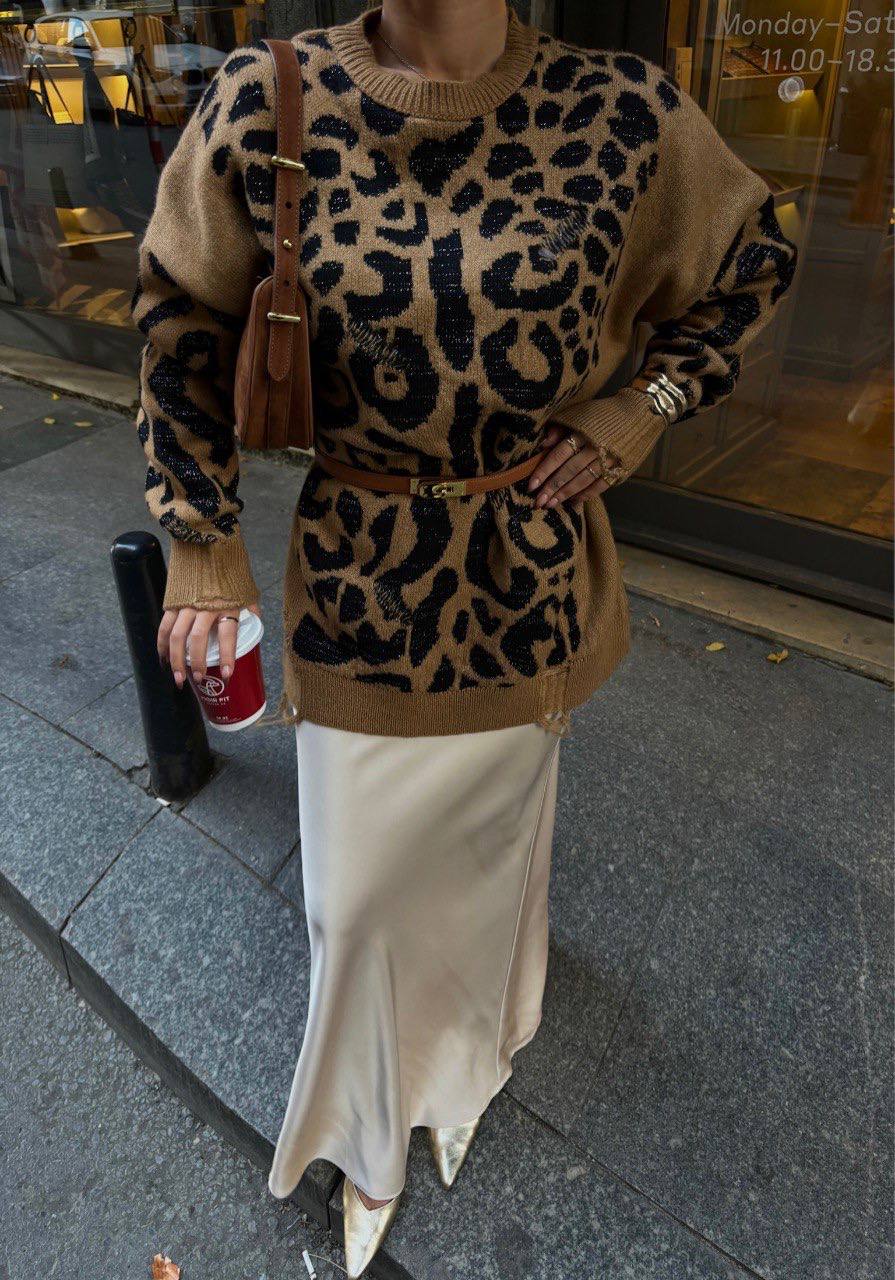 Person wearing a leopard print sweater and white skirt on a city street.