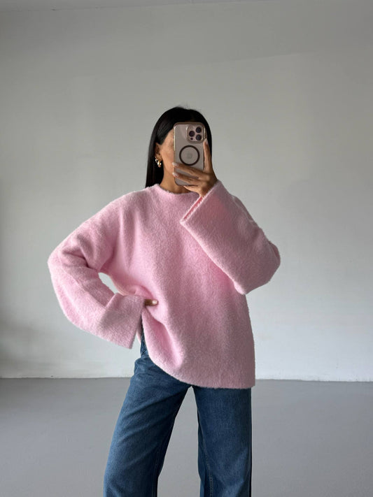 Person wearing a pink sweater and blue jeans taking a mirror selfie against a plain background