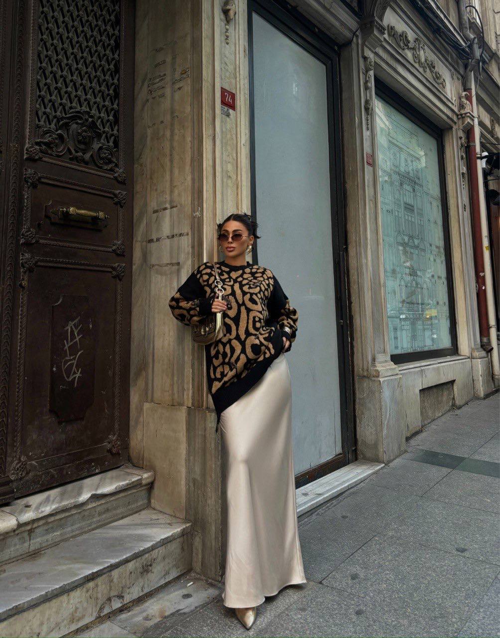 Woman in a patterned top and white skirt standing on a city street.