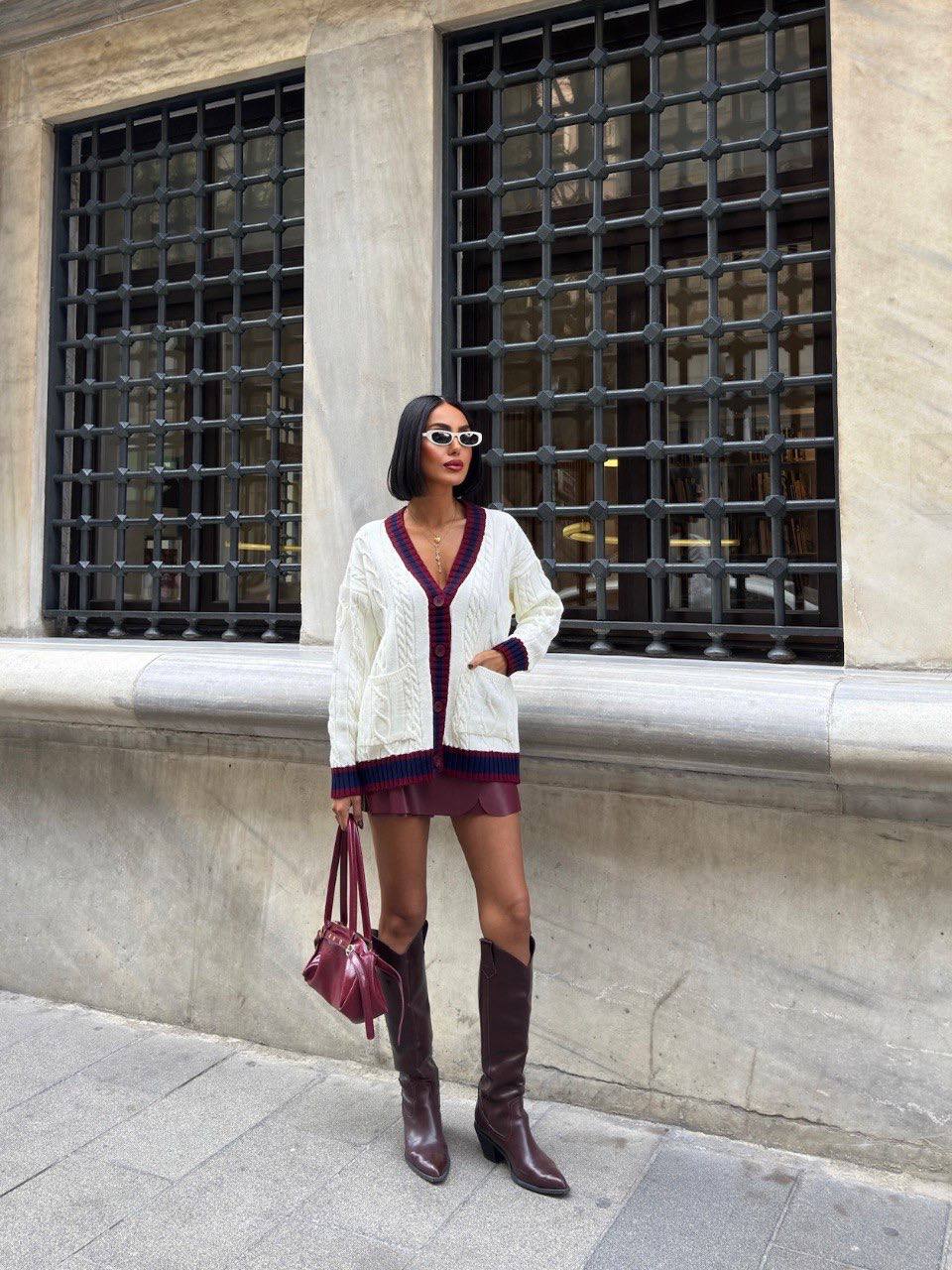 Woman in a white cardigan and burgundy dress standing in front of a building with large windows.