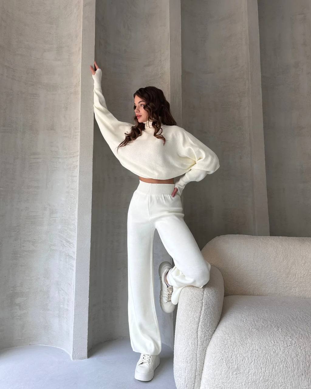 Woman in a white outfit posing against a neutral background