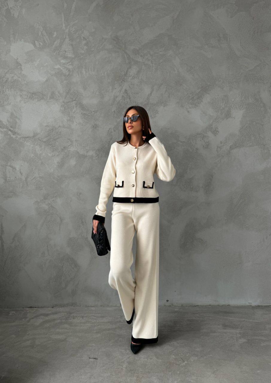 Woman in a white outfit with black accents against a gray textured wall.