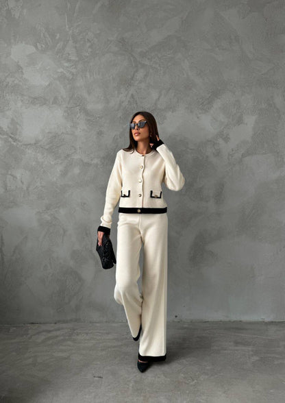 Woman in a white outfit with black accents against a gray textured wall.