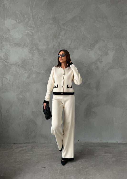 Woman in a white outfit with black accents against a gray textured wall.
