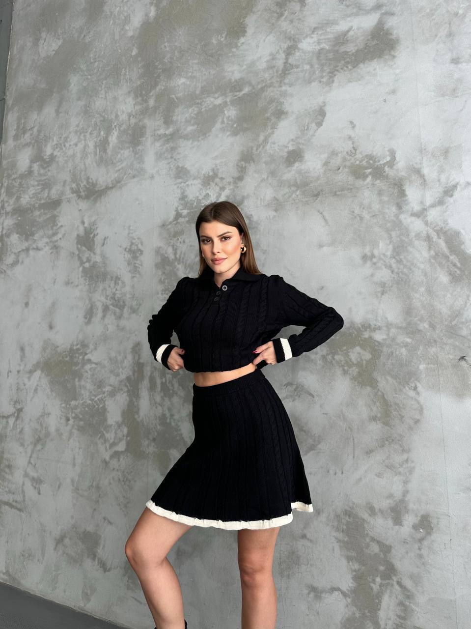 Woman wearing a black outfit with white trim against a textured gray wall