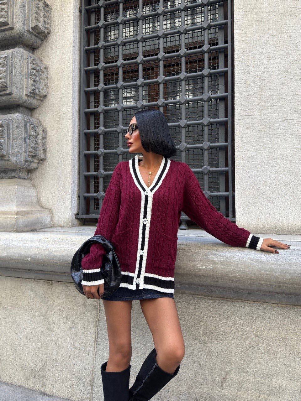 Woman wearing a burgundy cardigan with white and black accents, standing against a building wall.