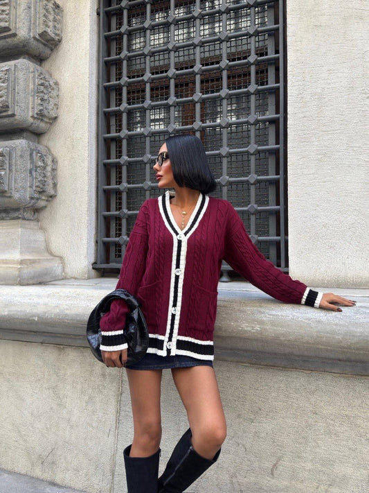 Woman wearing a burgundy cardigan with white and black accents, standing against a building wall.