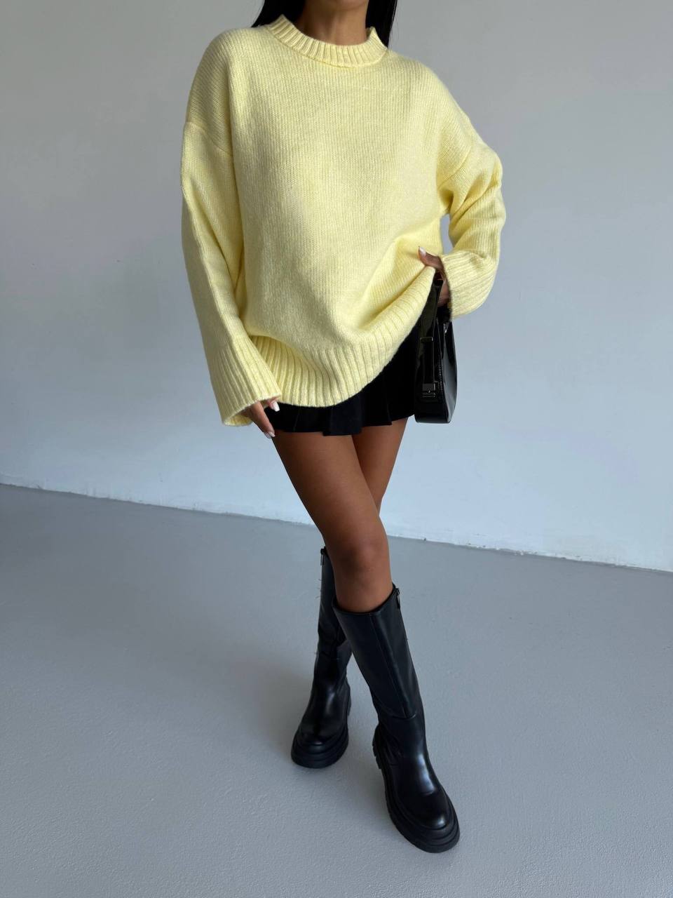 Person wearing a yellow sweater, black skirt, and black boots on a plain background