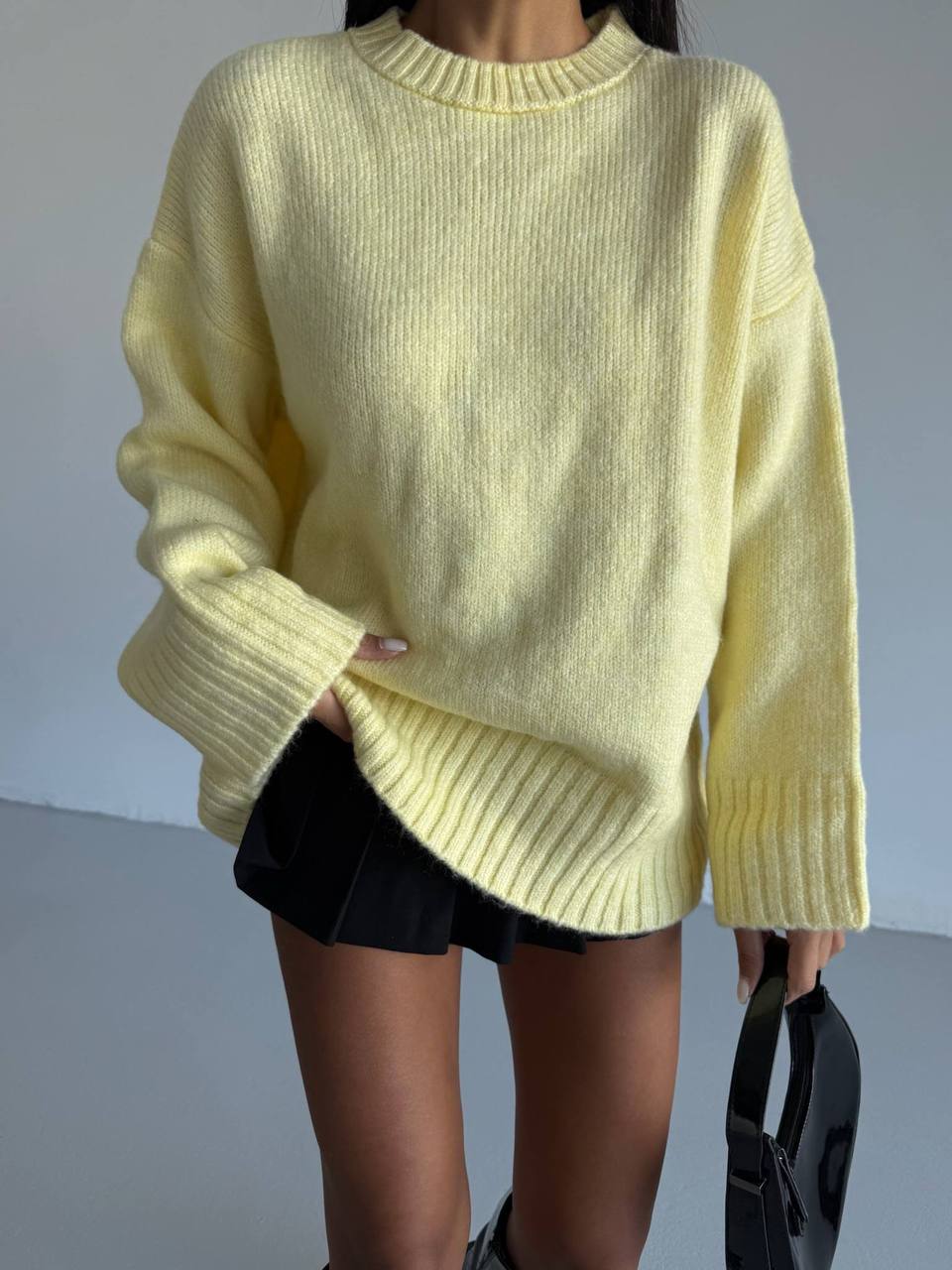 Person wearing a light yellow sweater and black shorts against a neutral background